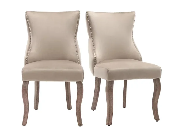 Juego de 2 sillas de terciopelo beige con patas curvas de madera marrón, botones decorativos y remaches plateados.